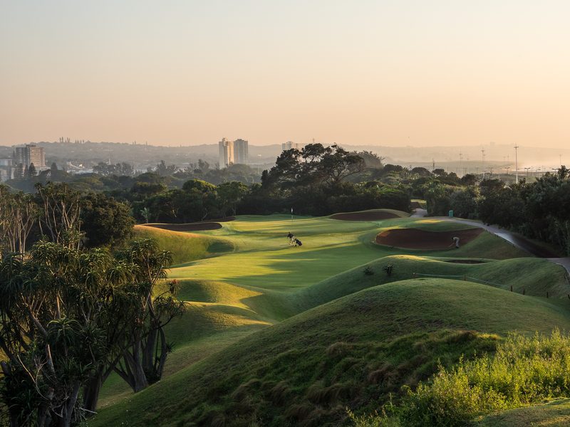 Rolling dune fairways at Durban Country Club at sunset, with the city skyline behind