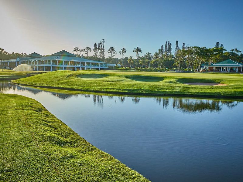 Green beside the water with the clubhouse behind at Mount Edgecombe Country Club