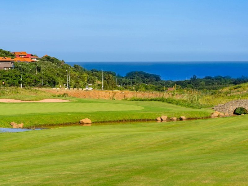 A fairway and stone bridge on the Ernie Els Signature Course at Zimbali Lakes, with the Indian Ocean behind