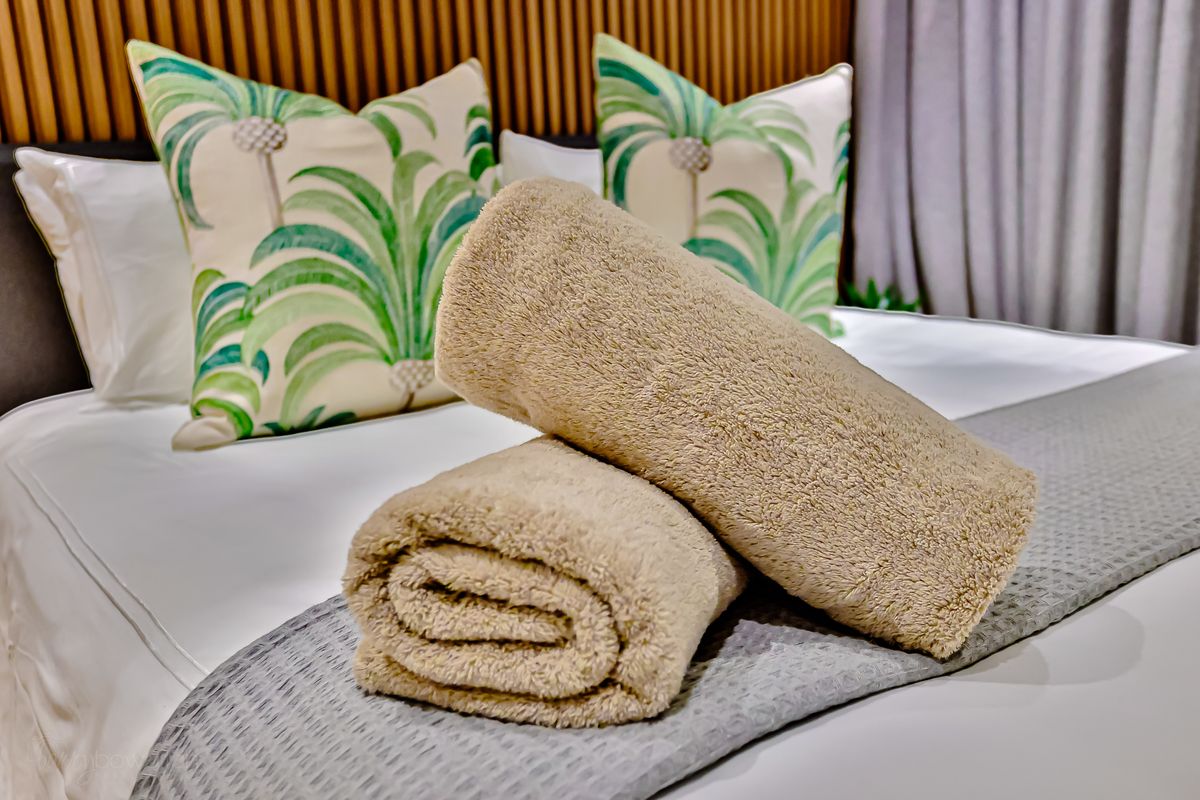 Rolled towels and palm-print cushions on the bed
